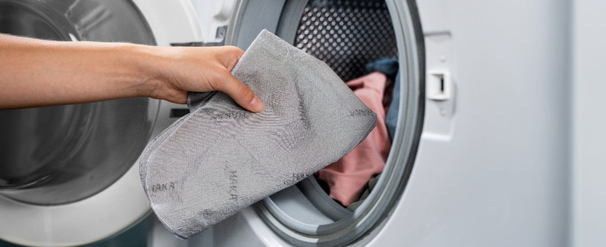 Hand legt Silbertuch in die Waschmaschine